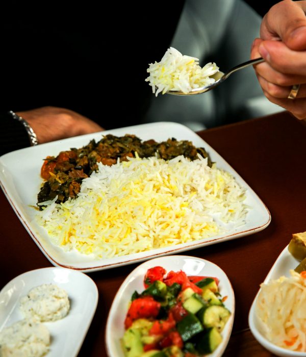 side view of rice with stewed meat and herbs on a wooden table